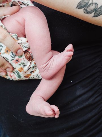 Close-up of a newborn baby's leg and foot held by a tattooed adult.