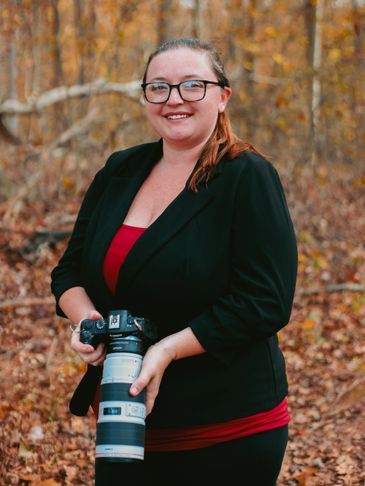 Woman in glasses holding a camera in a fall forest.