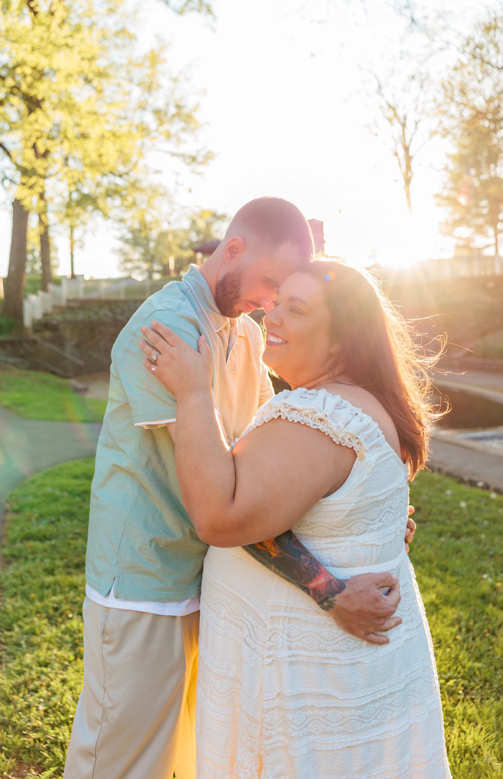 A couple embraces warmly outdoors with sunlight glowing behind them.