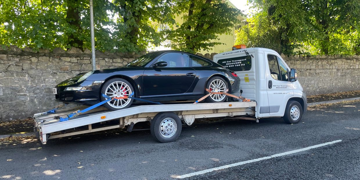 Black sports car secured on a white flatbed tow truck.