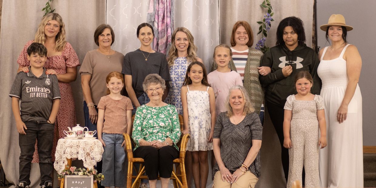 A diverse multi-generational family portrait with smiling faces and warm attire indoors.