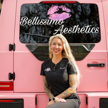 A woman with tattoos smiles, sitting in front of a pink van with 'Bellissimo Aesthetics' logo.