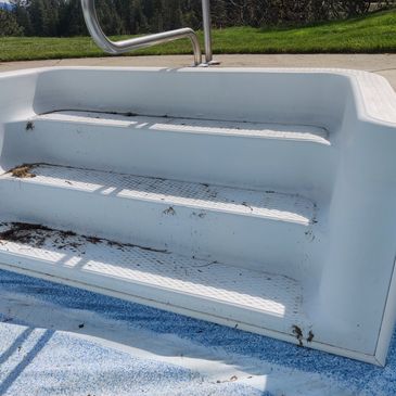 Dirty white pool steps with debris and a metal handrail.