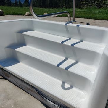 Three-step white fiberglass pool steps with metal handrail outdoors. The end results of a pool step repair and pool step painting project.