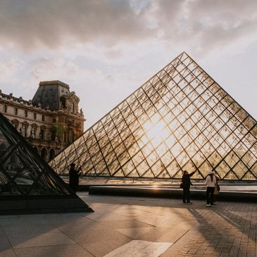 People near the glass pyramid at the Louvre in Paris during sunset.