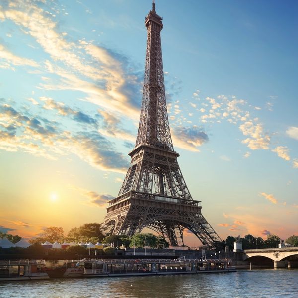 Eiffel Tower at sunset with a calm river and bridge in the foreground.