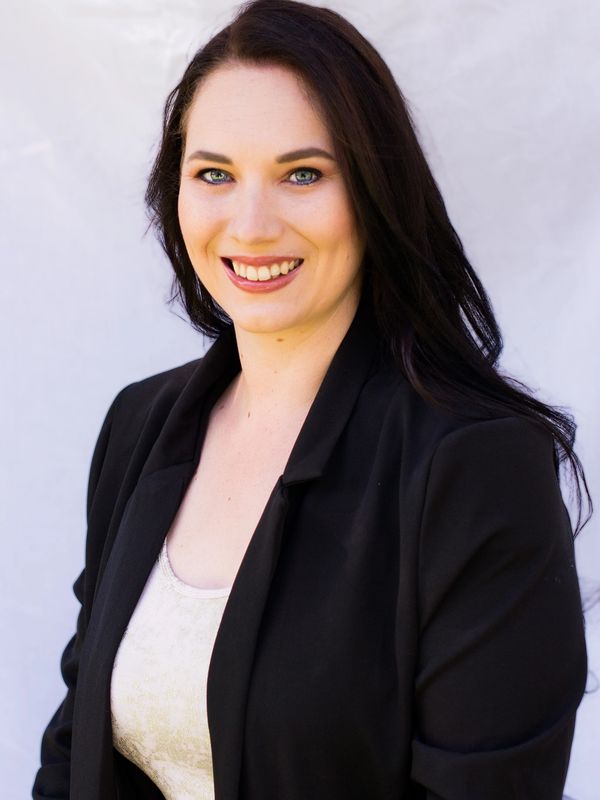 Smiling woman with dark hair in a black blazer and cream top against a light background.