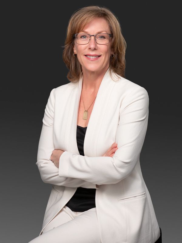 Professional woman in a white suit smiles confidently against a dark background.
