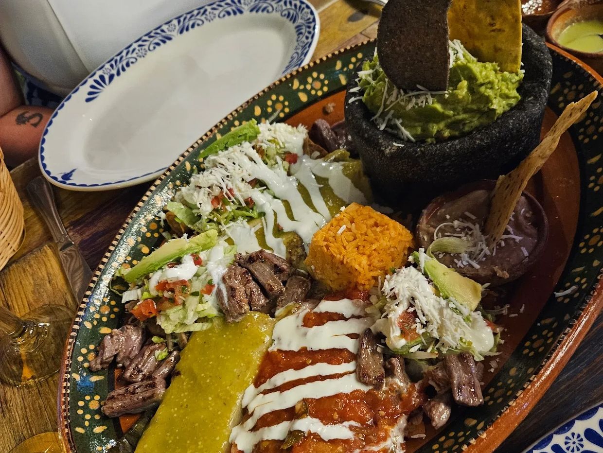 Traditional Mexican platter with tacos, rice, guacamole, and beans on a decorative plate.