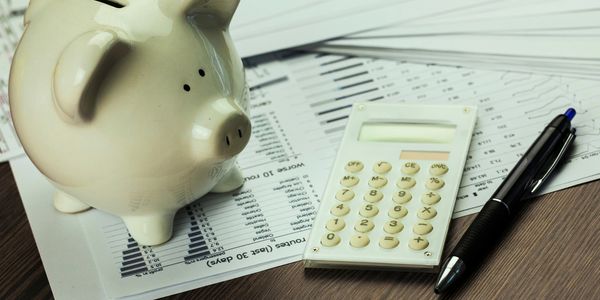 Coin bank shaped like a pig next to paper, pen, and calculator.