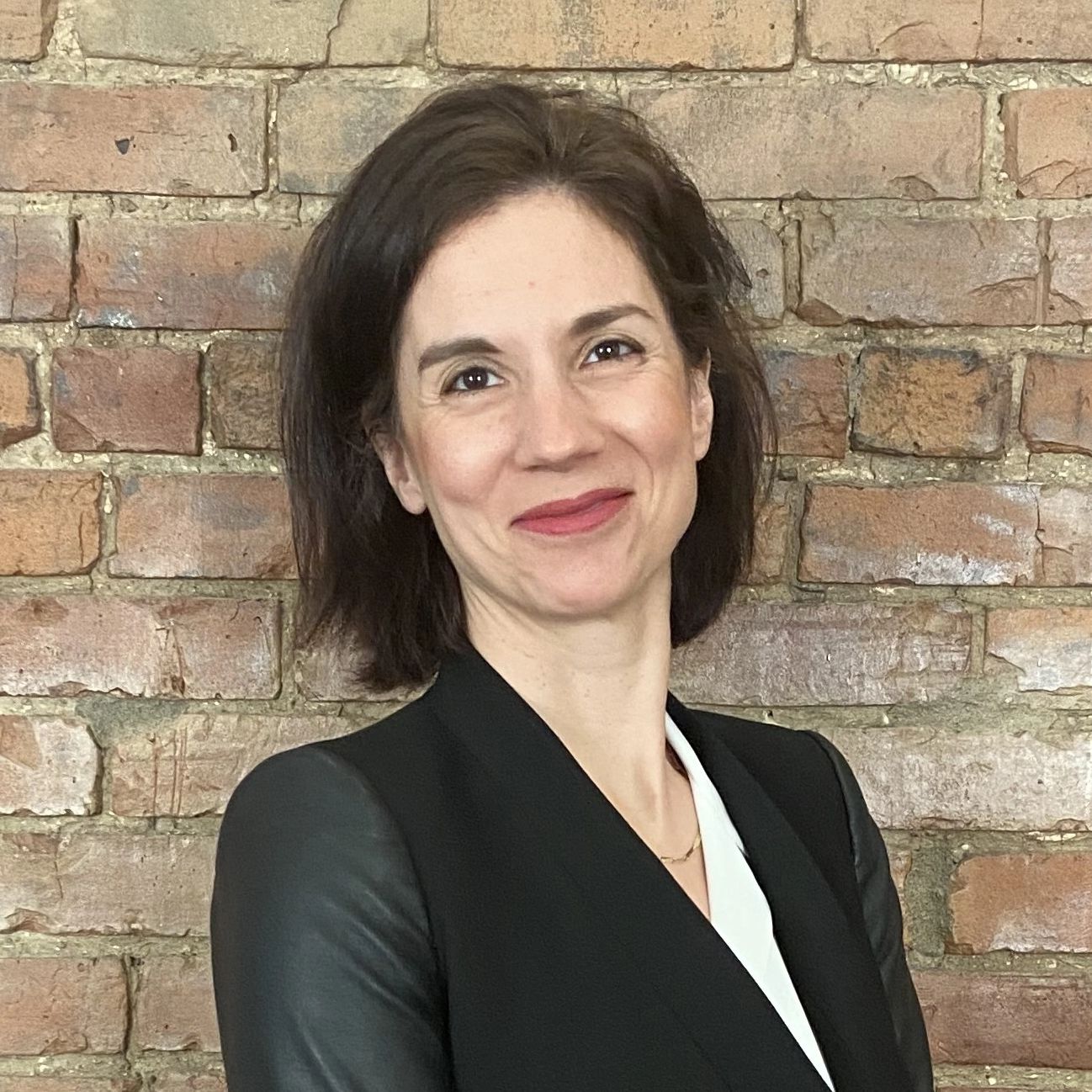 Confident woman smiling in front of a brick wall.