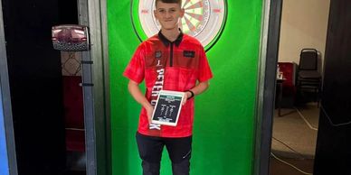 Young man in a red shirt holding a plaque in front of a dartboard.
