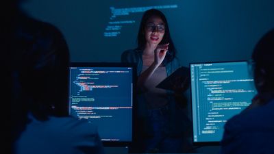 Woman leading a nighttime coding session with team members.