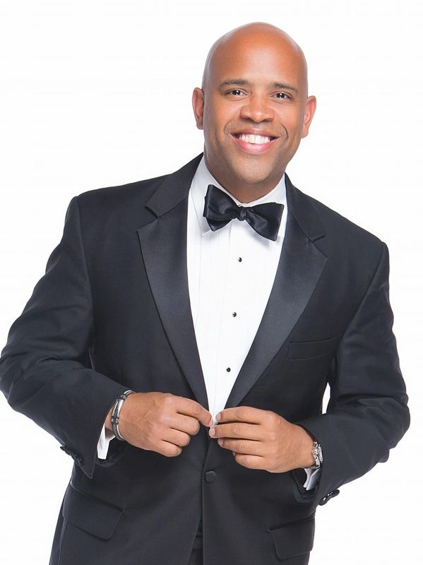 Man in a black tuxedo smiling at the camera.