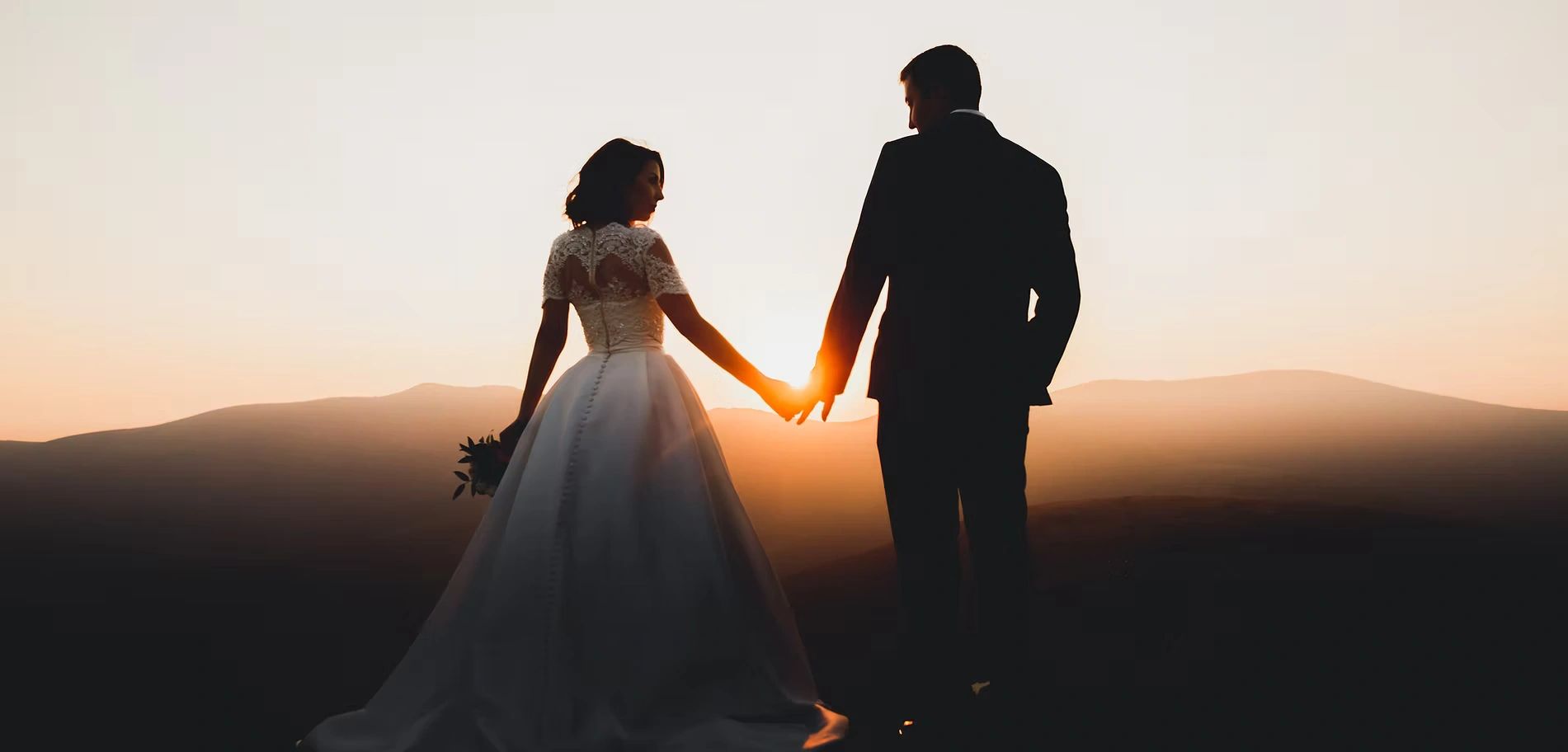 Silhouette of bride and groom holding hands at sunset.