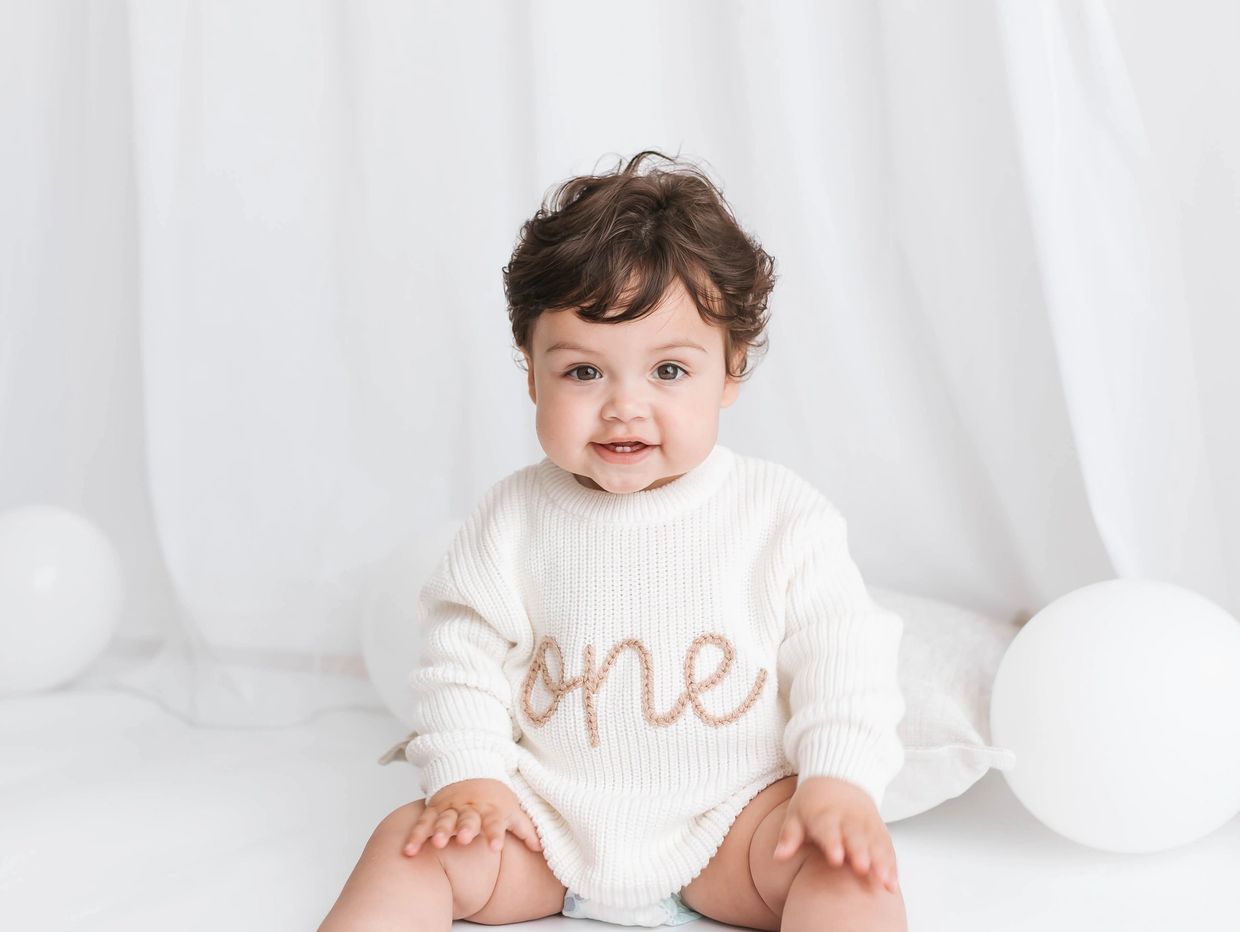 First birthday photoshoot in Milton Keynes, baby wearing white “one” jumper sitting with balloons.