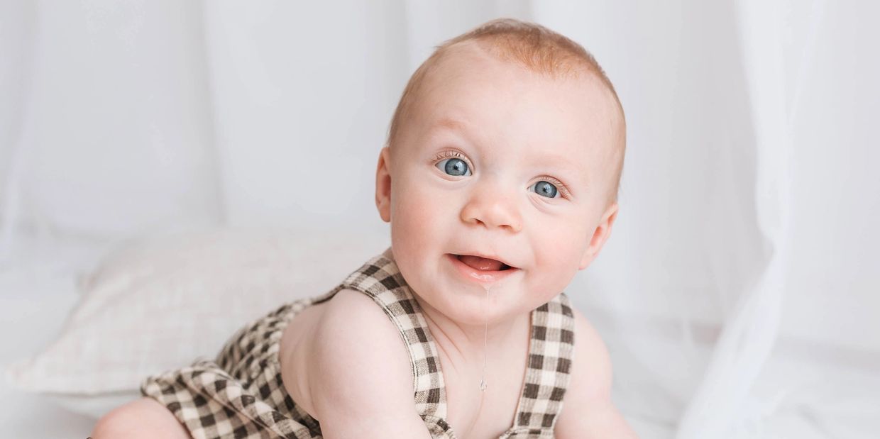 Smiling baby boy in check romper holding wooden toy during sitter session in Milton Keynes