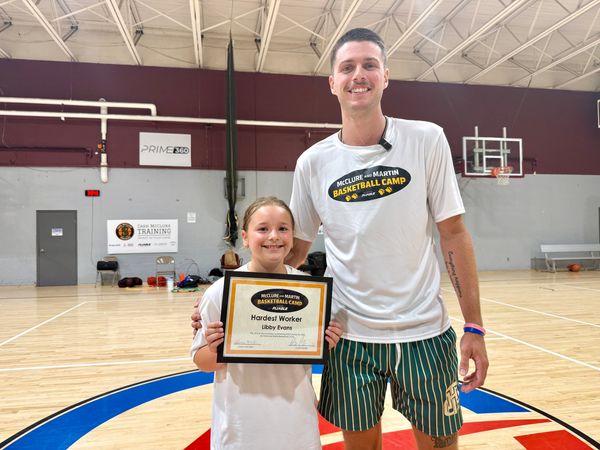 Young girl receiving basketball camp award with coach.