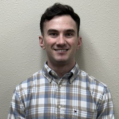 Young man smiling in plaid shirt against beige wall.
