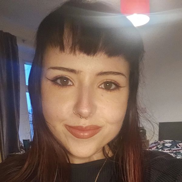 Young woman with long hair and a nose ring smiling indoors.