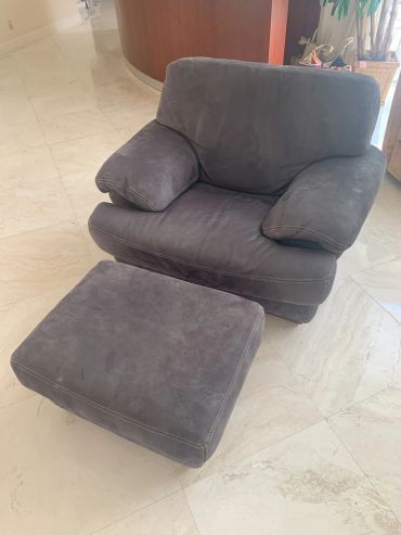 Comfortable dark gray armchair with matching ottoman on marble floor.