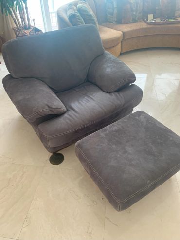 Gray cushioned armchair with matching ottoman on marble floor.