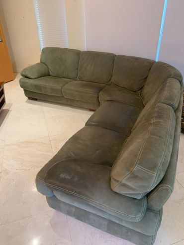 Large green suede L-shaped sectional sofa in a bright room.