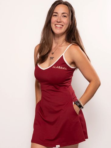 Smiling woman wearing a red Alabama dress with hands in pockets.