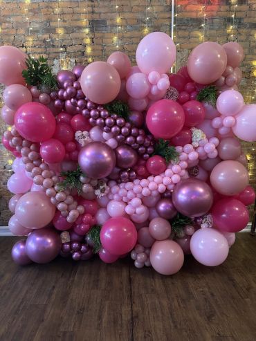 Pink and purple balloon arrangement with greenery on wooden floor.