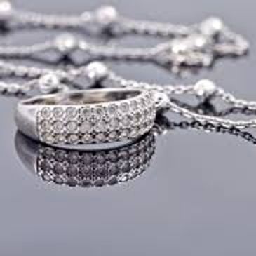 A silver ring with small diamonds and a chain necklace on a reflective surface.