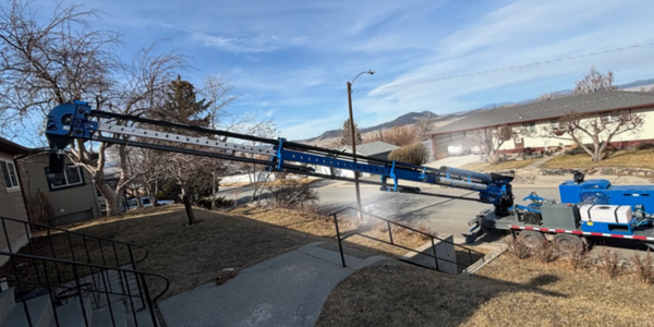 A long blue crane extending from a truck to a house.