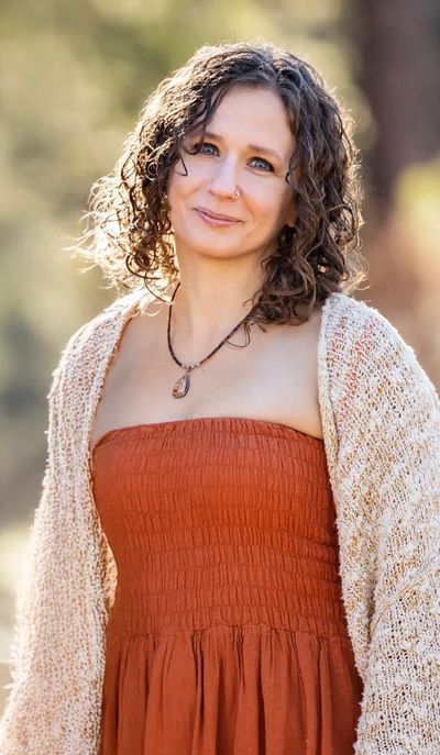 Woman with curly hair in an orange dress and knitted cardigan outdoors.
