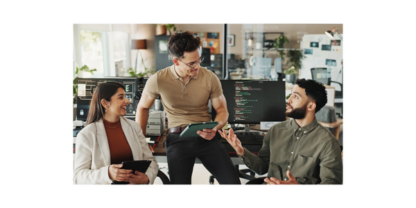 Three colleagues discussing work in a modern office with computers and tablets.