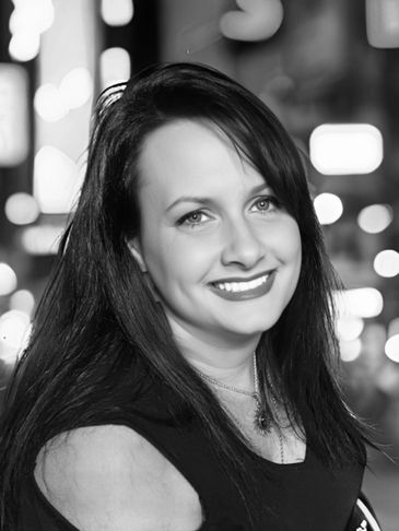 Black and white portrait of a smiling woman with long hair and a necklace.