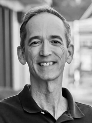 Smiling middle-aged man in a black polo shirt outdoors.