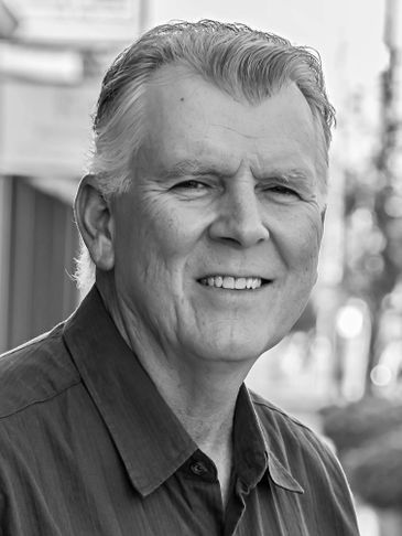 Smiling elderly man in a casual shirt, captured in black and white.