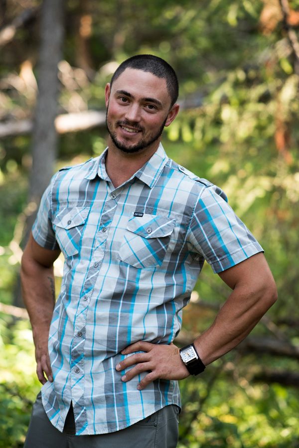 Man in a plaid shirt smiling outdoors with hands on hips.