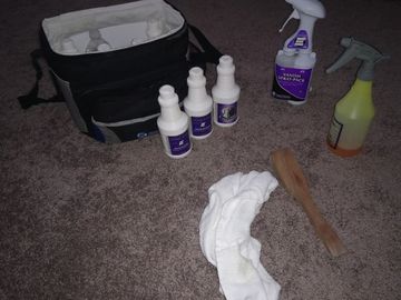 Cleaning supplies including sprays, bottles, a wooden spatula, and cloth on carpet.