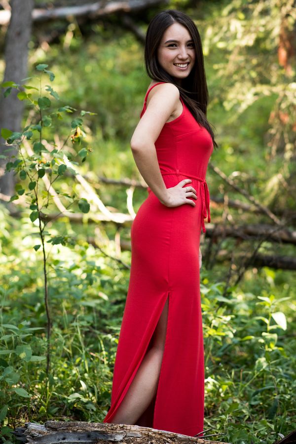 Woman in a red dress smiling in a forest setting.