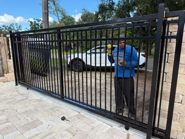 Man cleaning or maintaining a black iron gate outdoors.