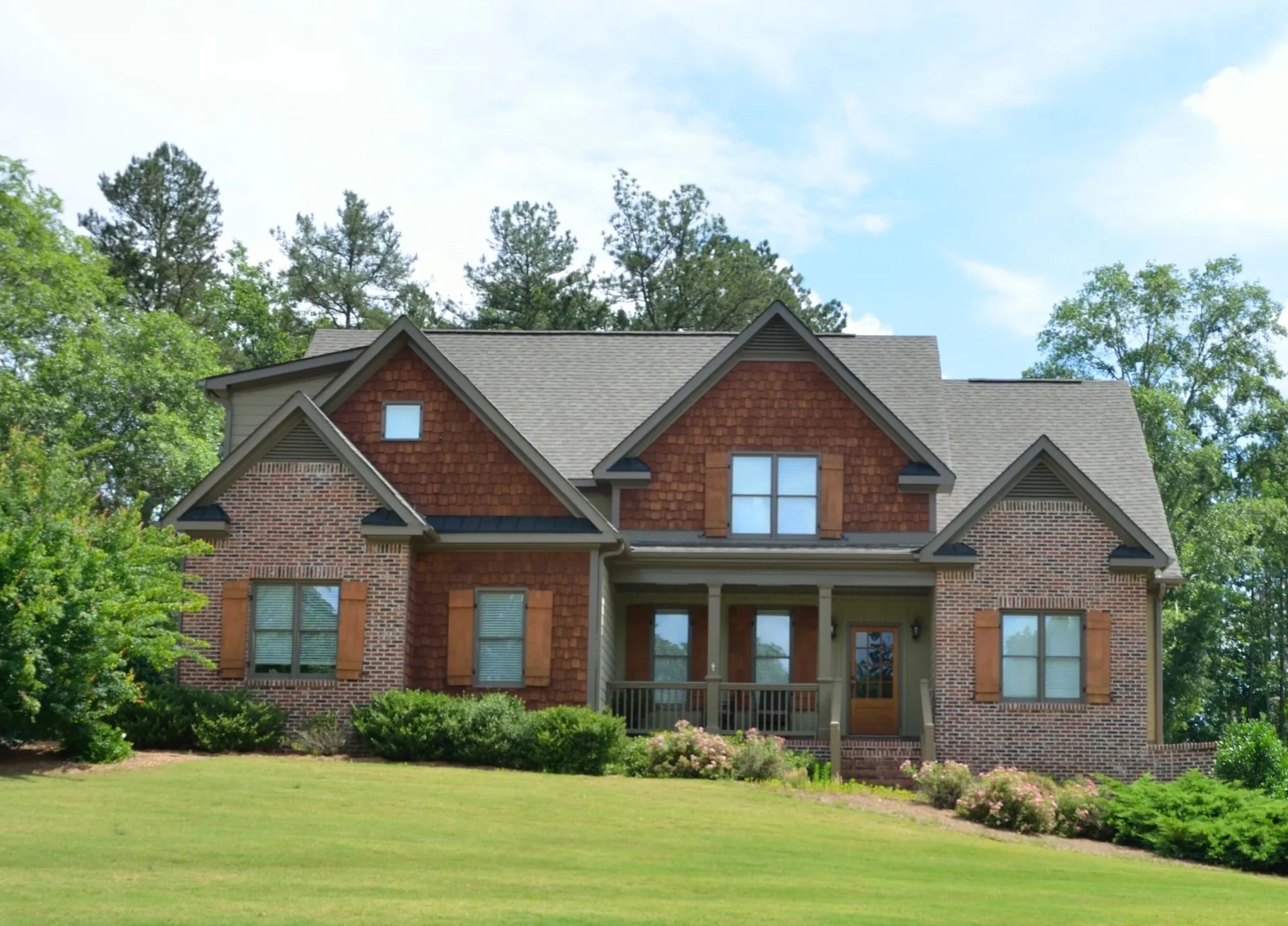 A brick and wood house with a green lawn and trees in the background.
