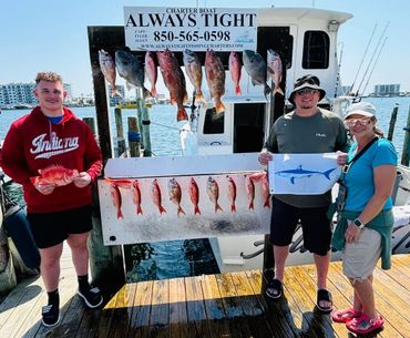 Three people proudly displaying their fresh catch on a dock under a charter boat sign.