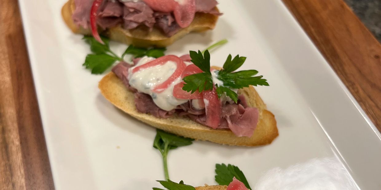 In-house seared & roasted beef atop a crisp baguette, finished with crème fraîche and pickled onion.