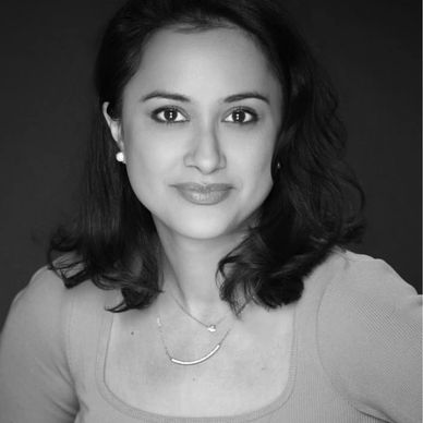 Portrait of a woman with dark hair wearing a pink top and delicate jewelry.