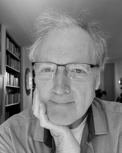 Older man with glasses resting his chin on his hand in a cozy room.