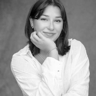 Young woman smiling softly, resting her chin on her hand in a black and white portrait.