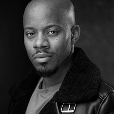 Confident man with a shaved head wearing a black jacket and green shirt.