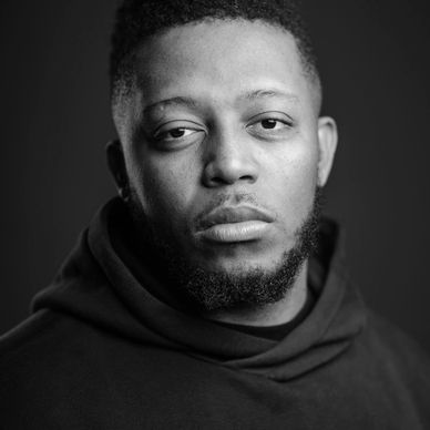 Close-up portrait of a serious young man with a beard and black hoodie.