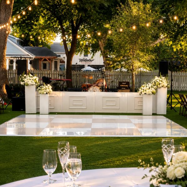 Outdoor wedding stage with white dance floor and floral decorations.