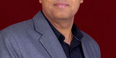 Man wearing a gray blazer and black shirt, smiling slightly.